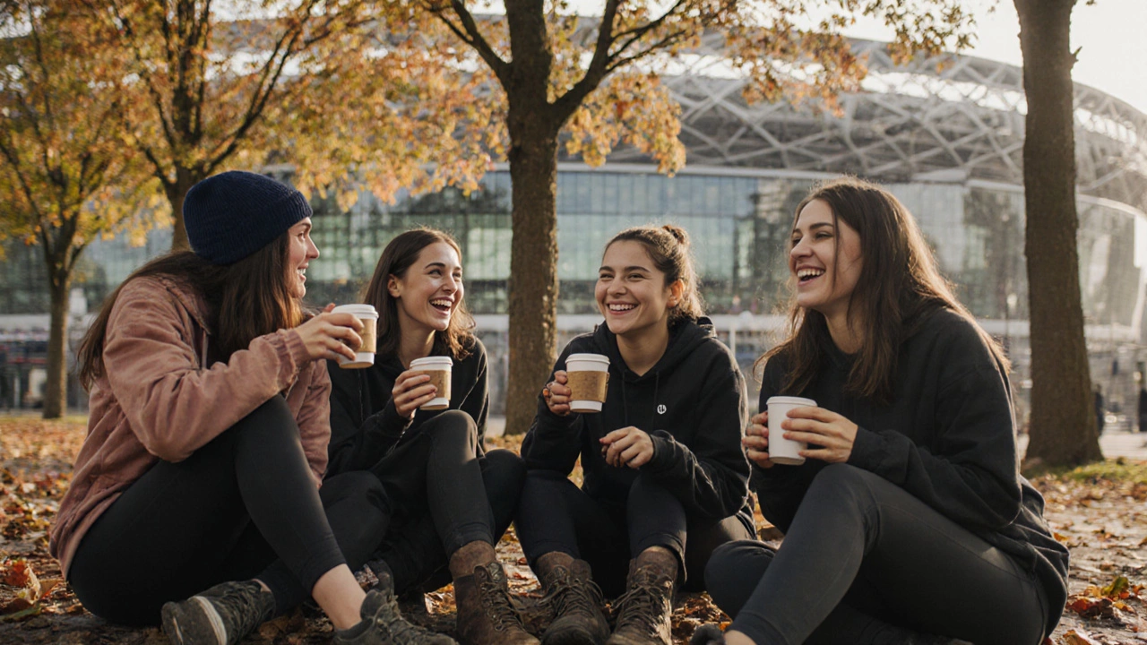 A group of women laughing over coffee after a morning workout outside a stadium.