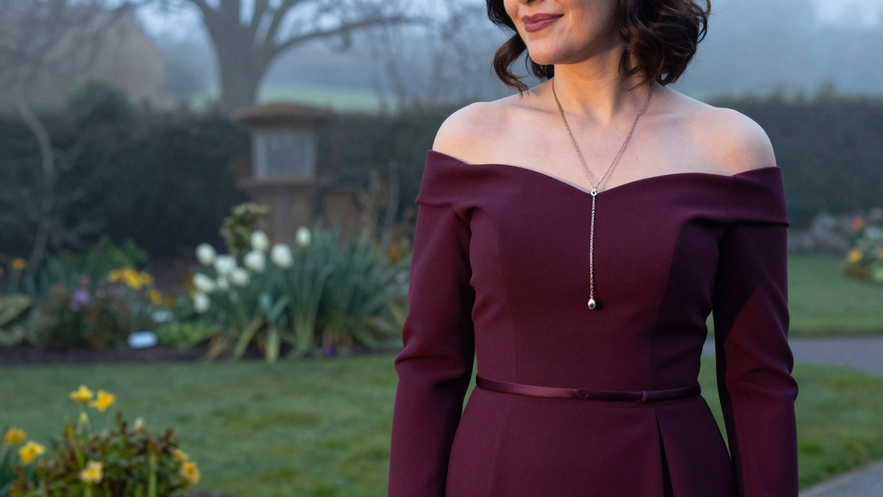 An Irish woman in a deep plum off-shoulder gown smiling beside a misty garden, with a long pendant necklace enhancing her silhouette.