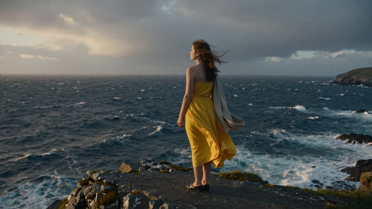 Woman in a yellow dress standing on a windy Irish cliff edge holding a beige cardigan